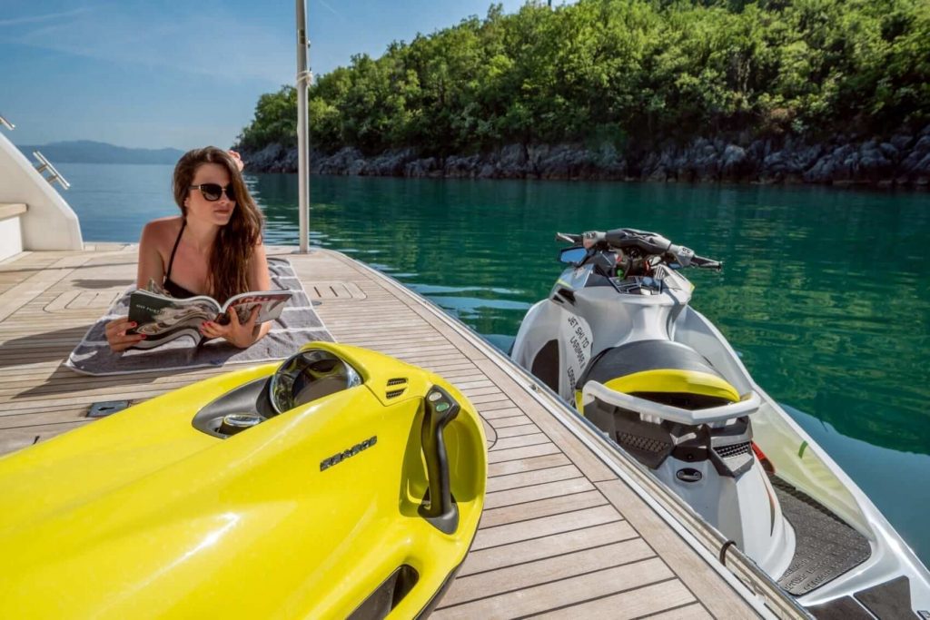 girl is sunbathing on a yacht charter by two jet skis