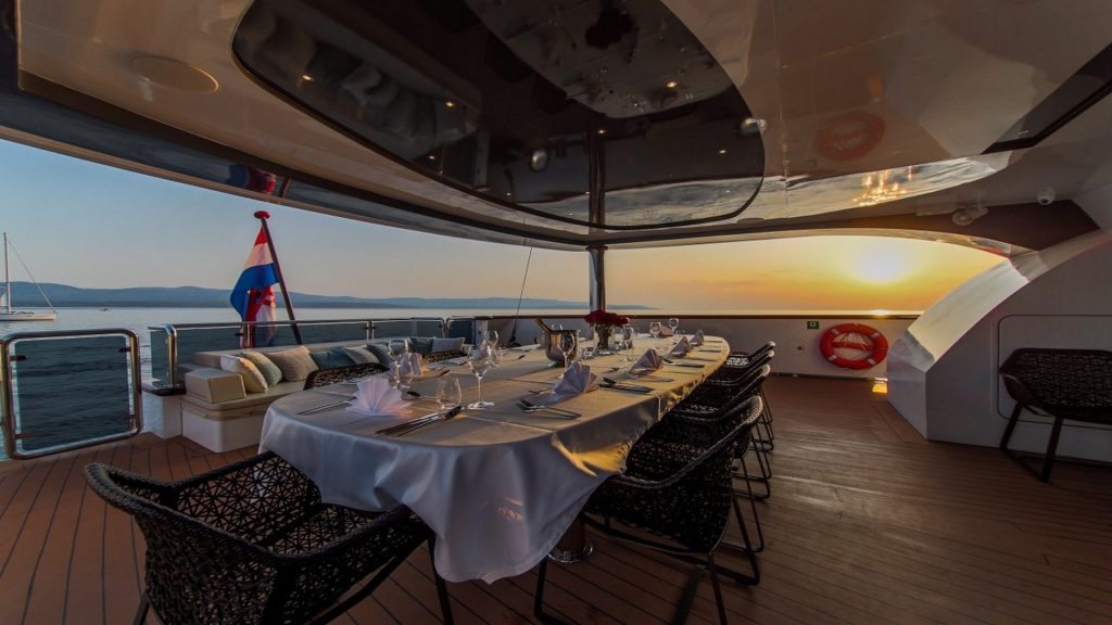 aiaxaia yacht charter large table on a main deck served for dinner during sunset