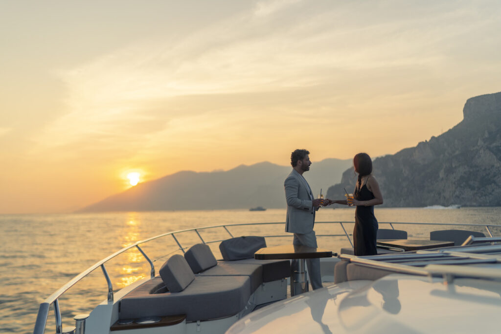 two guests on a yacht front deck with a sunset in the background