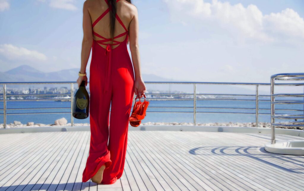 lady on a superyacht deck carrying a bottle of champagne & high heels